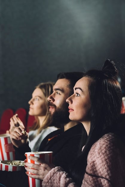 A movie theater showing several people watching a movie on the big screen while eating popcorn - audience is obscured