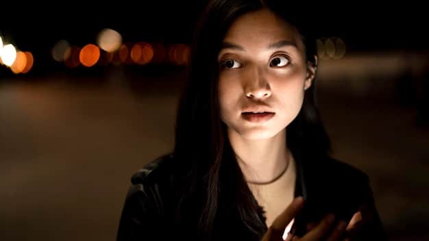 A close-up shot of a female protagonist in a thriller K-drama. She has a determined expression, and the lighting is dramatic, with shadows emphasizing the tension in the scene. In the background, a blurred cityscape hints at the urban setting of the drama.