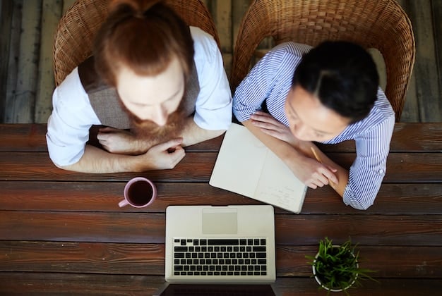 Two people sitting at a table, collaborating on translating a script. Close-up view with soft lighting. Books and a laptop on the desk, emphasizing teamwork and knowledge.