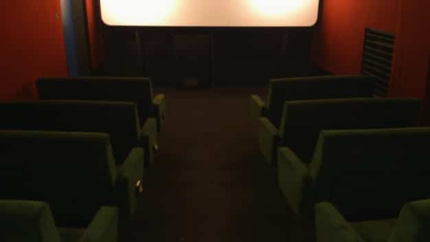 An empty movie theater with rows of empty seats. The scene is dimly lit, conveying a sense of decline due to the rise of streaming services. The focus is on the deserted atmosphere to highlight the impact on traditional cinema.